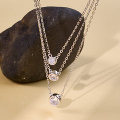 Three silver necklaces with crystal pendants on a stone surface for women