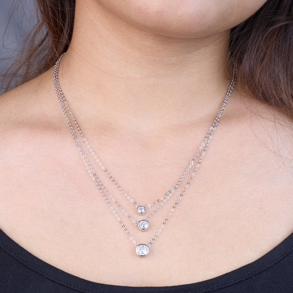 Close-up of a person wearing two silver necklaces with small round pendants.