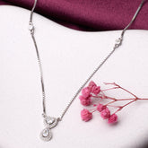 Silver necklace with a teardrop pendant on a white surface with pink flowers.