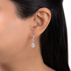 A close-up of a model's ear wearing a teardrop-shaped silver dangle earring with a halo of small clear stones and a central pear-cut gemstone.