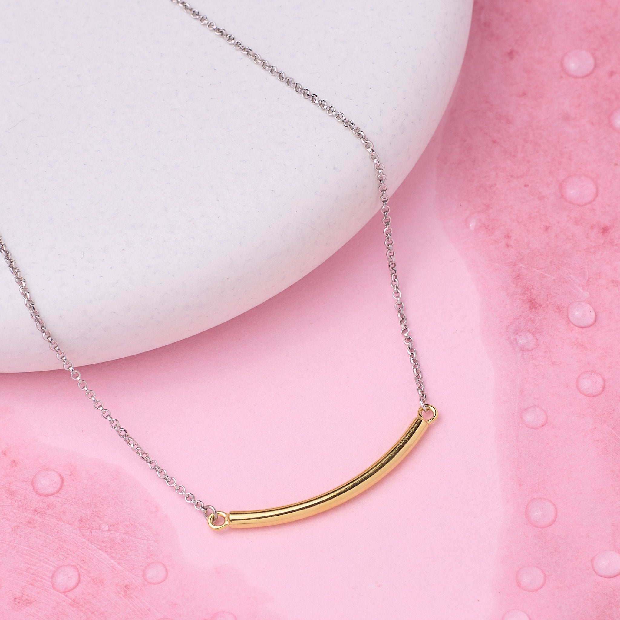 Gold curved bar necklace on a pink textured surface
