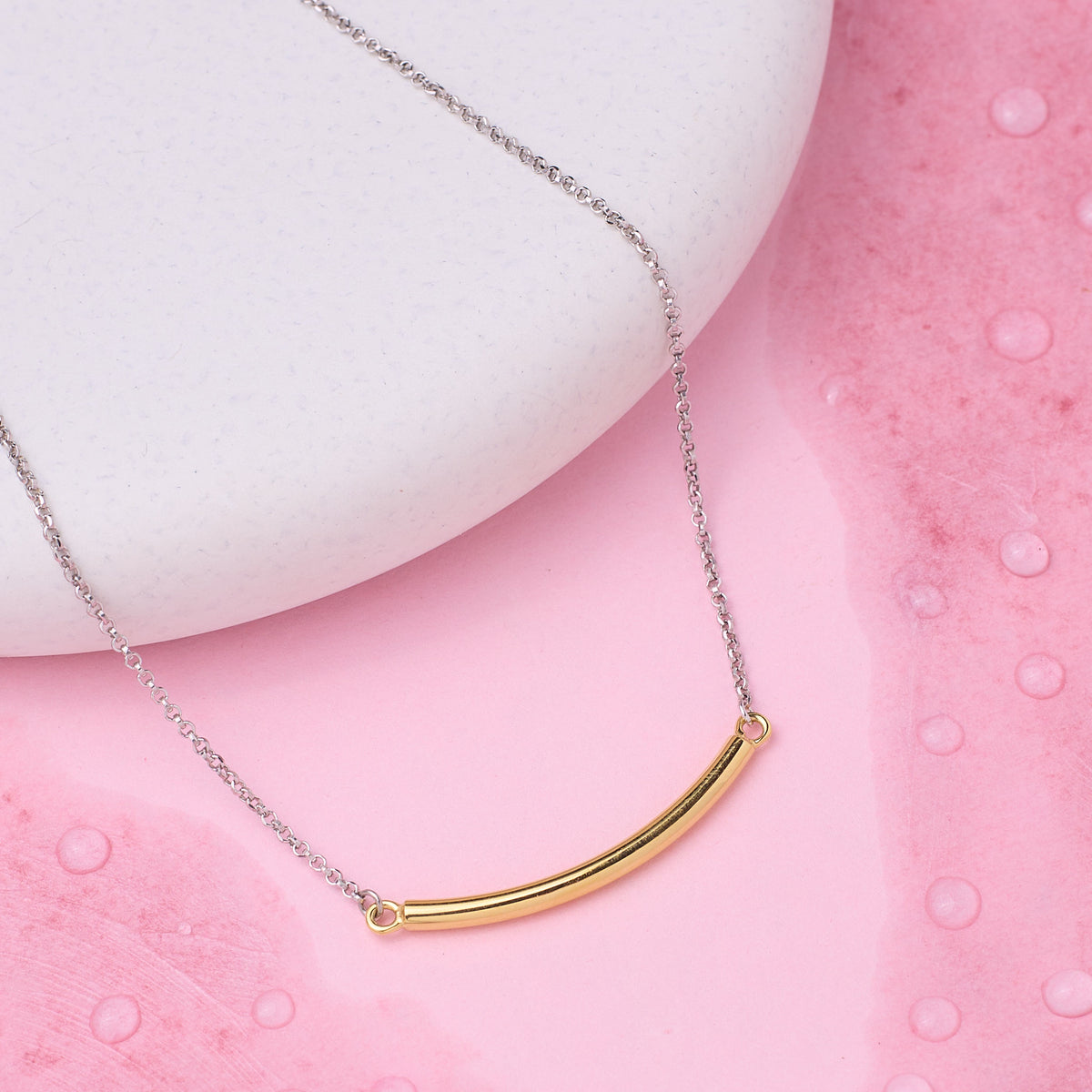 Gold curved bar necklace on a pink textured surface