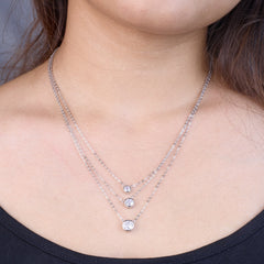 Close-up of a person wearing two silver necklaces with small round pendants.