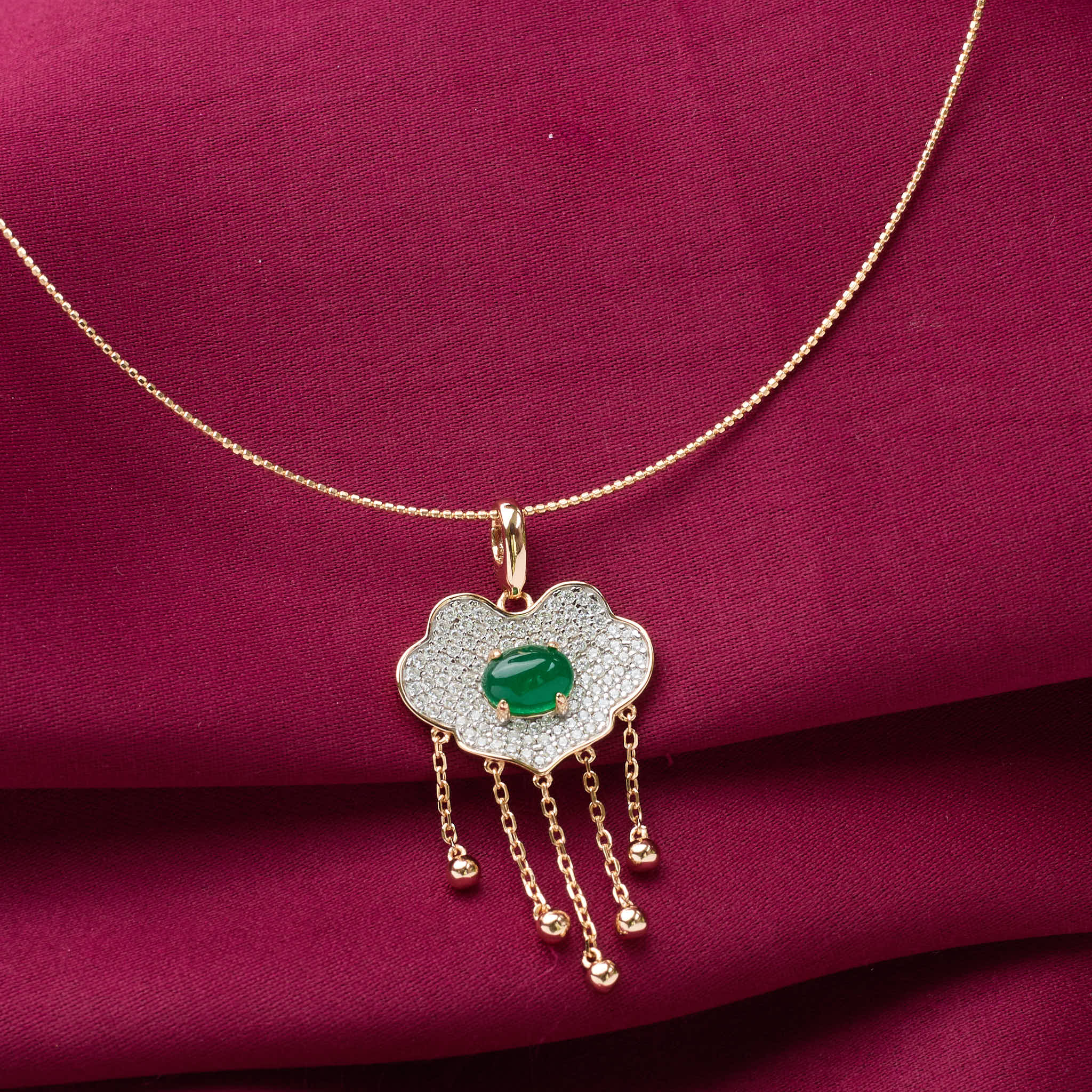 Gold necklace with a cloud-shaped pendant featuring a green gemstone on a red fabric background