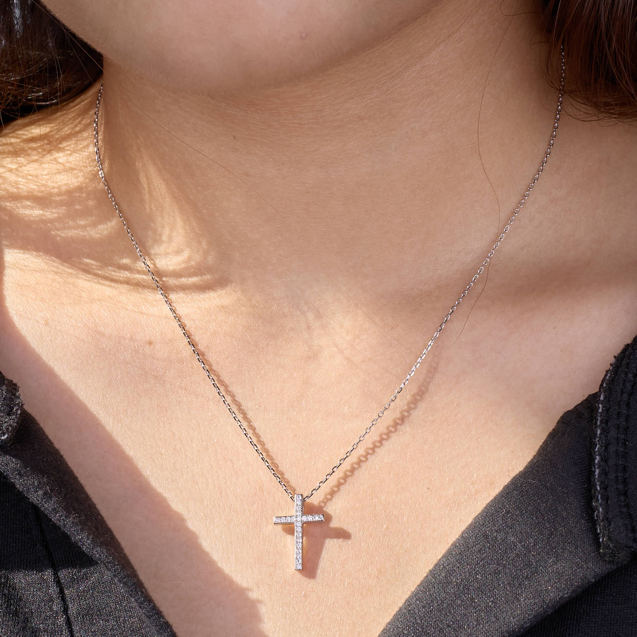 Person wearing a 925 silver cross necklace on a plain background