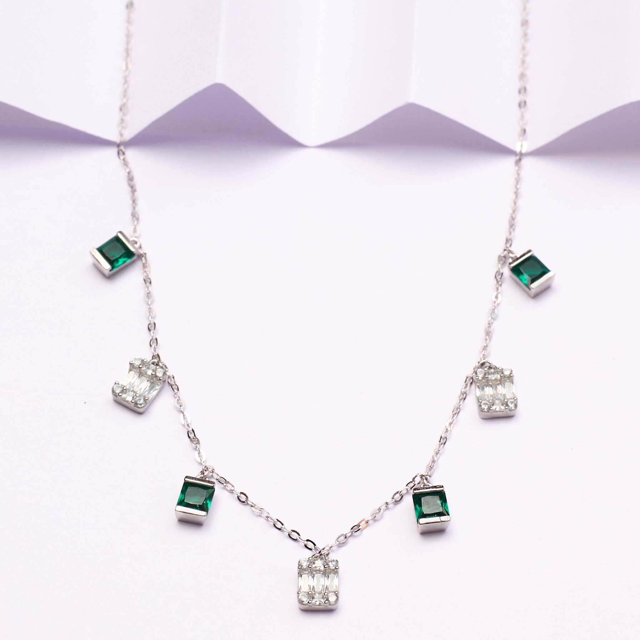Silver necklace with green gemstones on a white background