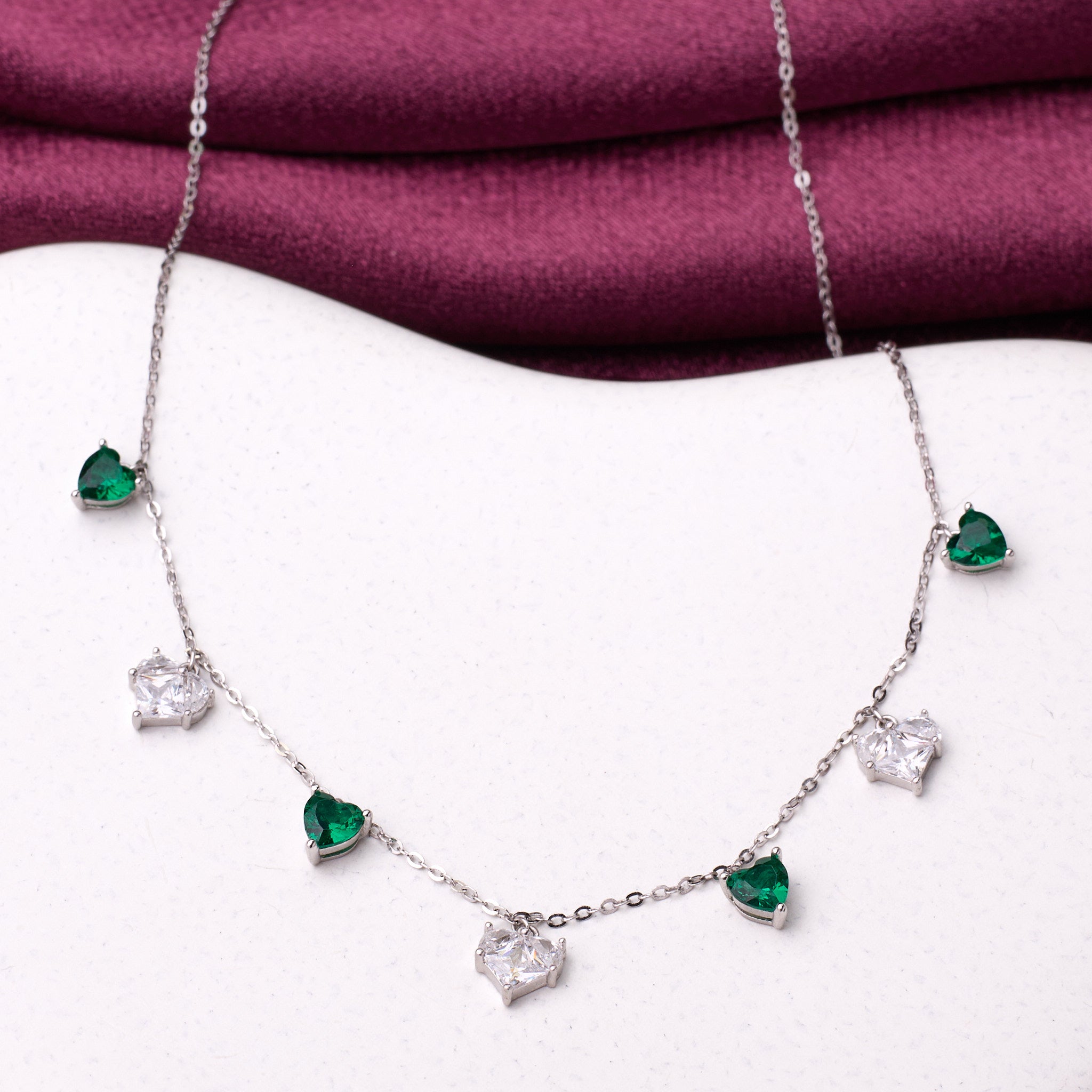 925 silver Necklace with heart-shaped emerald and diamond pendants on a white surface with a purple fabric background