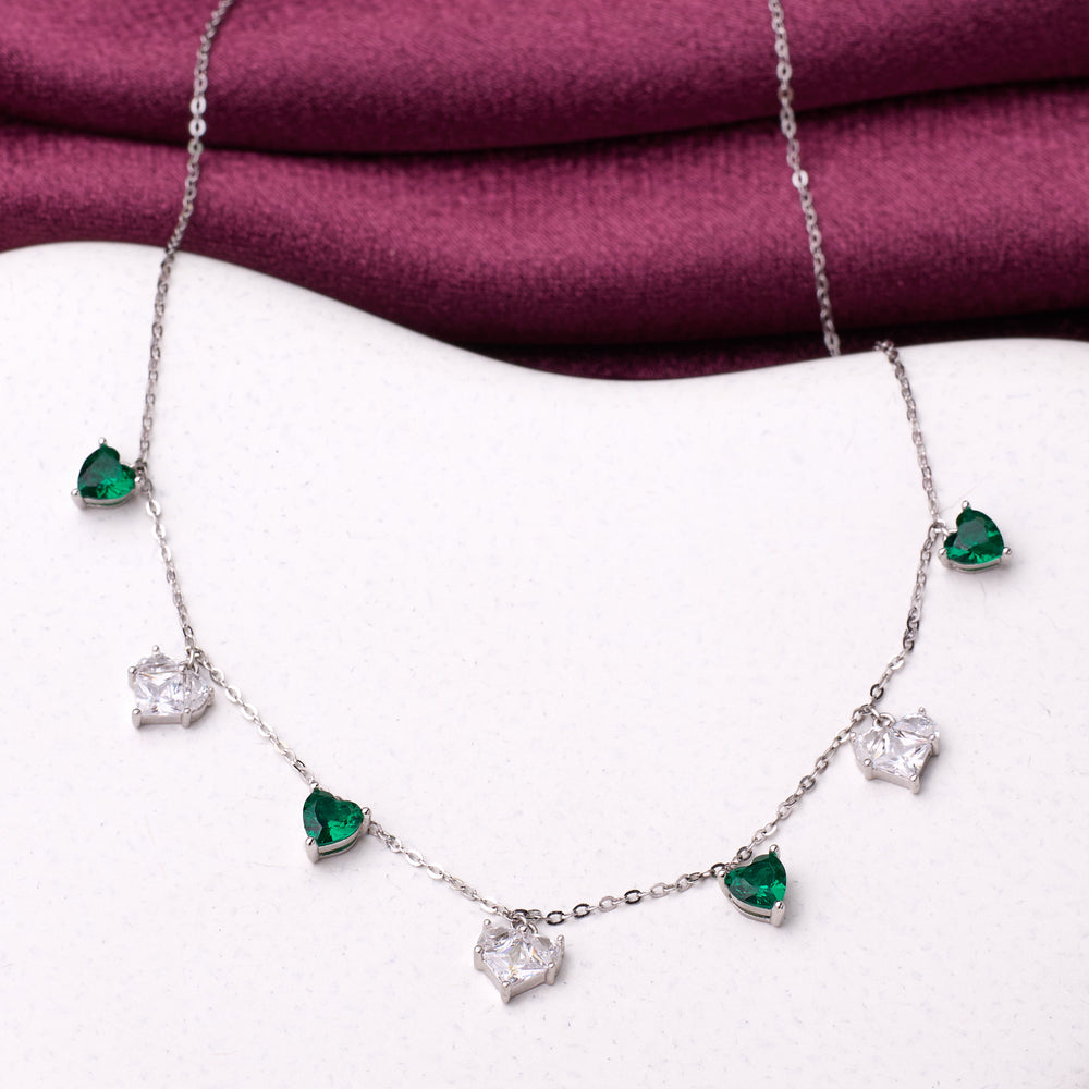 925 silver Necklace with heart-shaped emerald and diamond pendants on a white surface with a purple fabric background