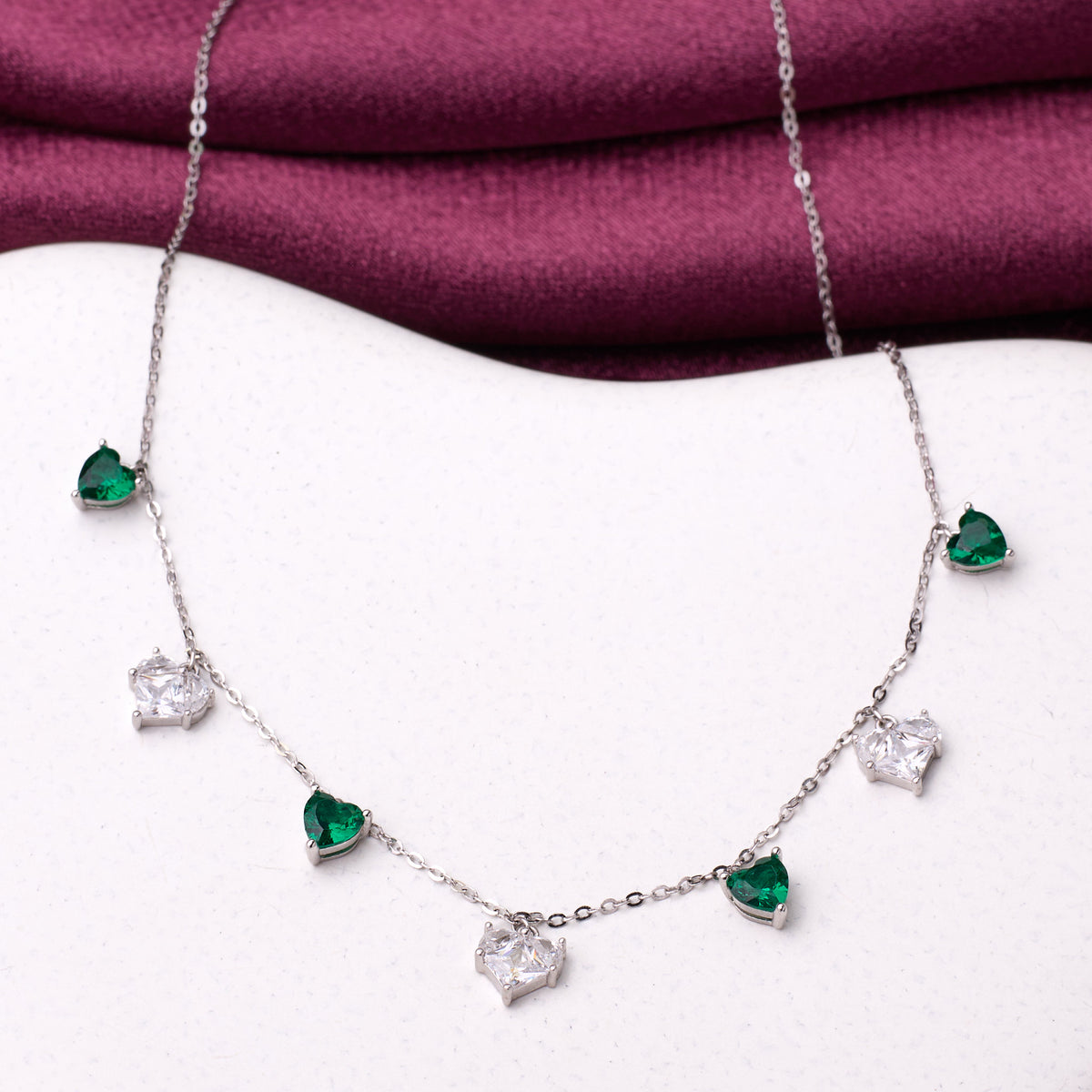 925 silver Necklace with heart-shaped emerald and diamond pendants on a white surface with a purple fabric background