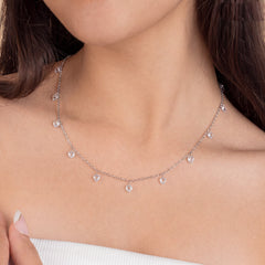 Woman wearing a 925 sterling silver charm necklace featuring multiple dangling heart-shaped American Diamond stones, 925 silver dangling heart American Diamond necklace