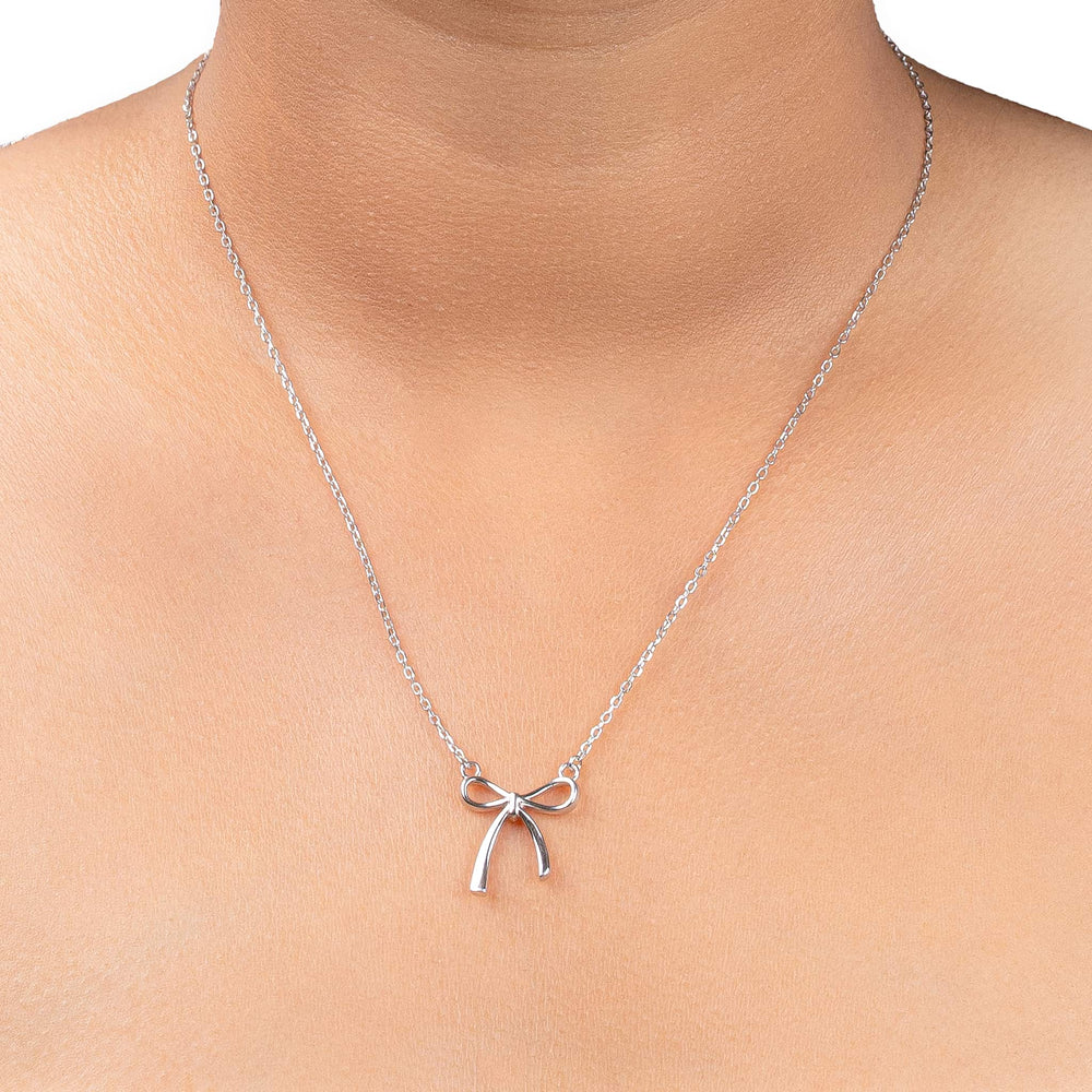 A delicate silver chain necklace with a small bow-shaped pendant, shown worn on a model's neck against a clean white background.